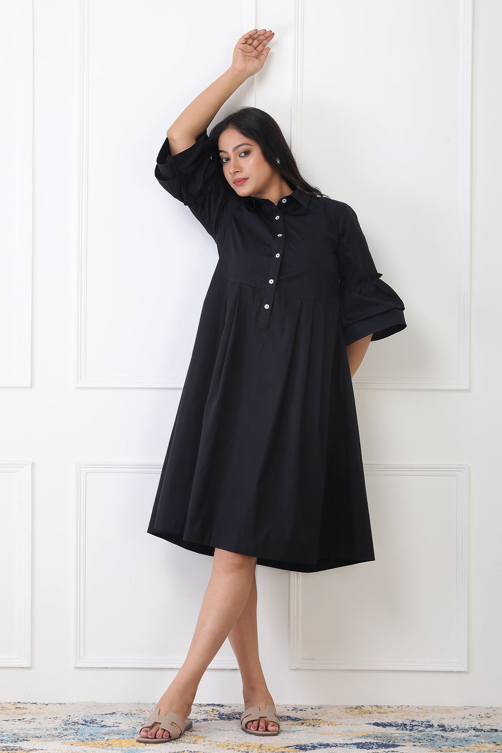 Woman wearing a black dress against a white paneled wall