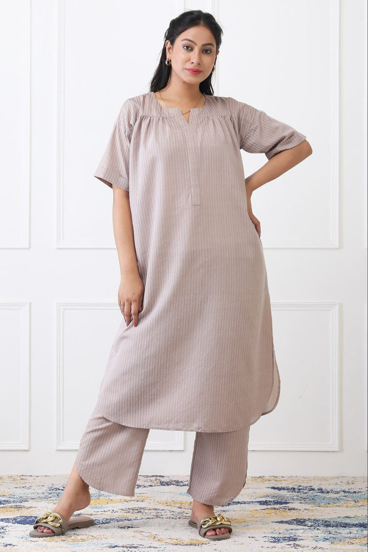 Woman wearing a beige dress with matching pants against a white wall.