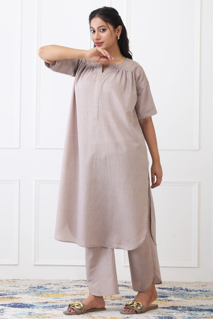 Woman wearing a beige kurta with palazzo pants against a white wall.