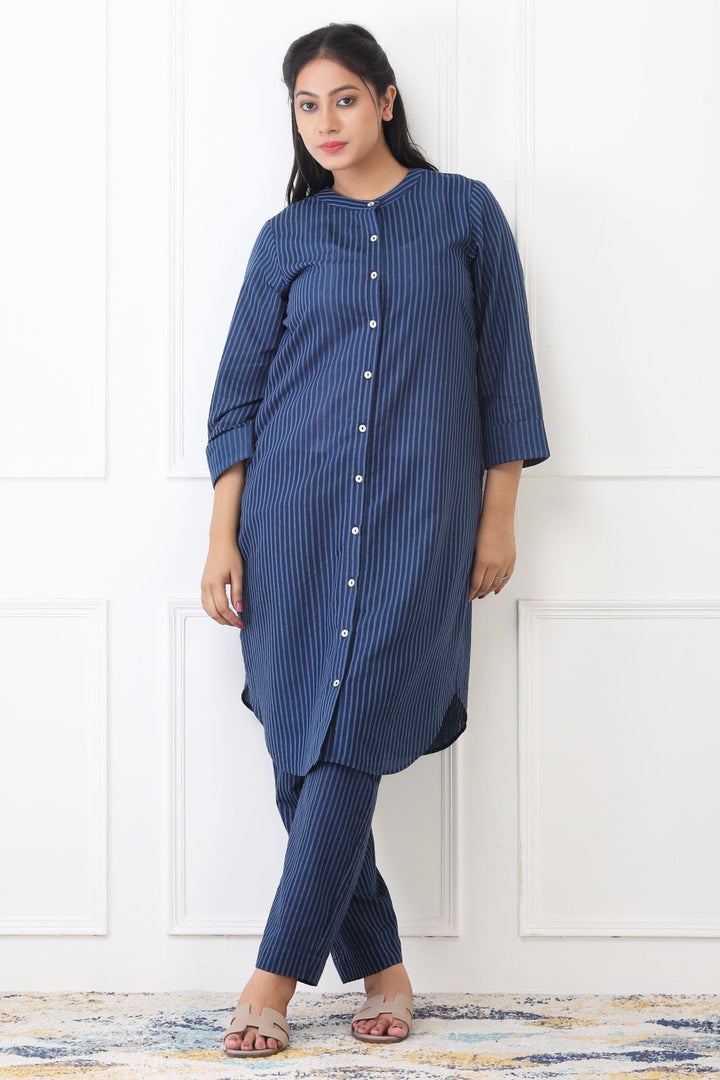 Woman wearing a blue striped kurta with pants against a white wall.