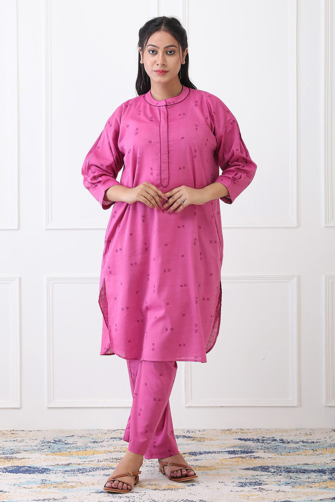 Woman wearing a pink kurta with pants against a white paneled wall.