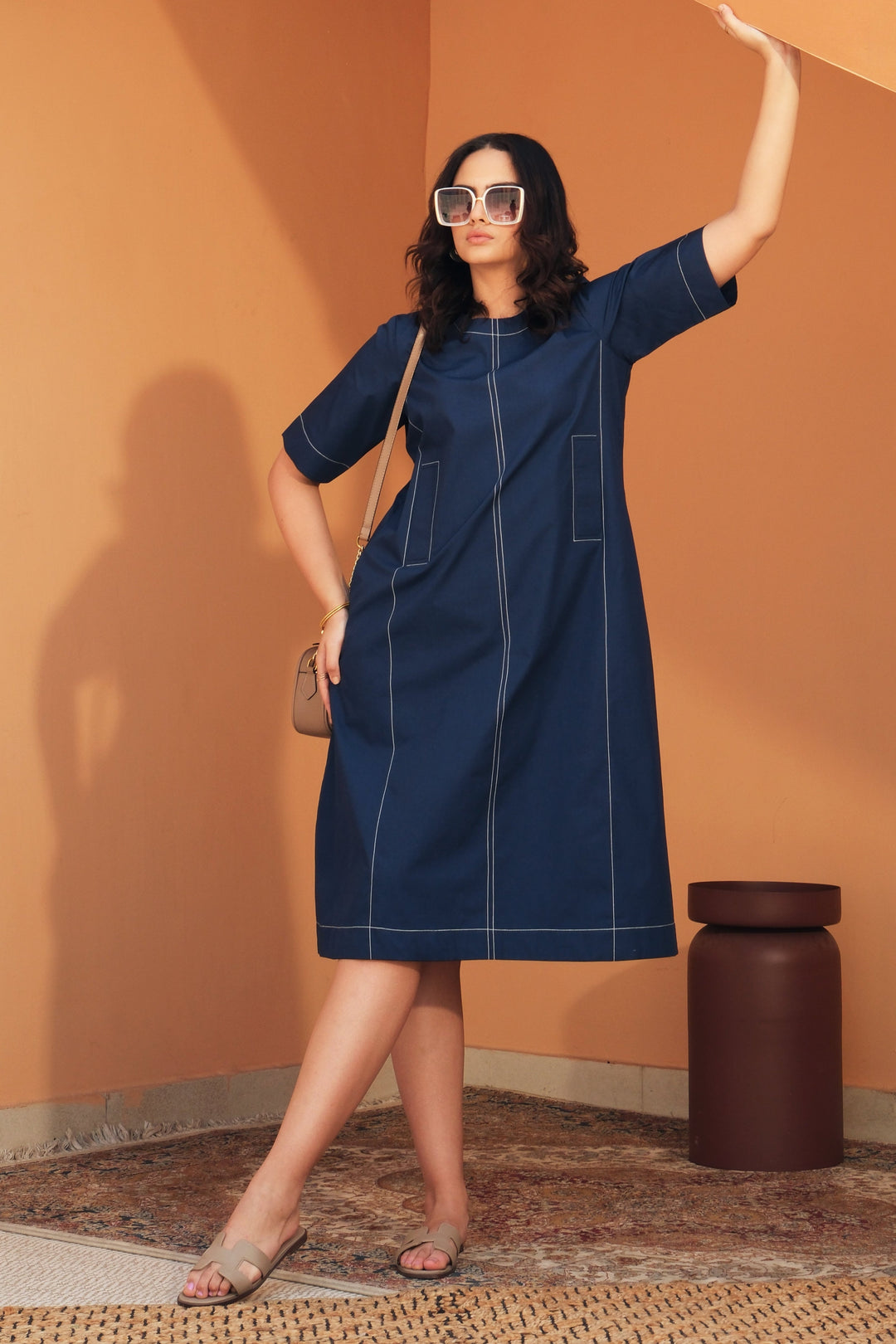 Woman wearing the Noa navy cotton midi dress with contrast cross-stitch detailing