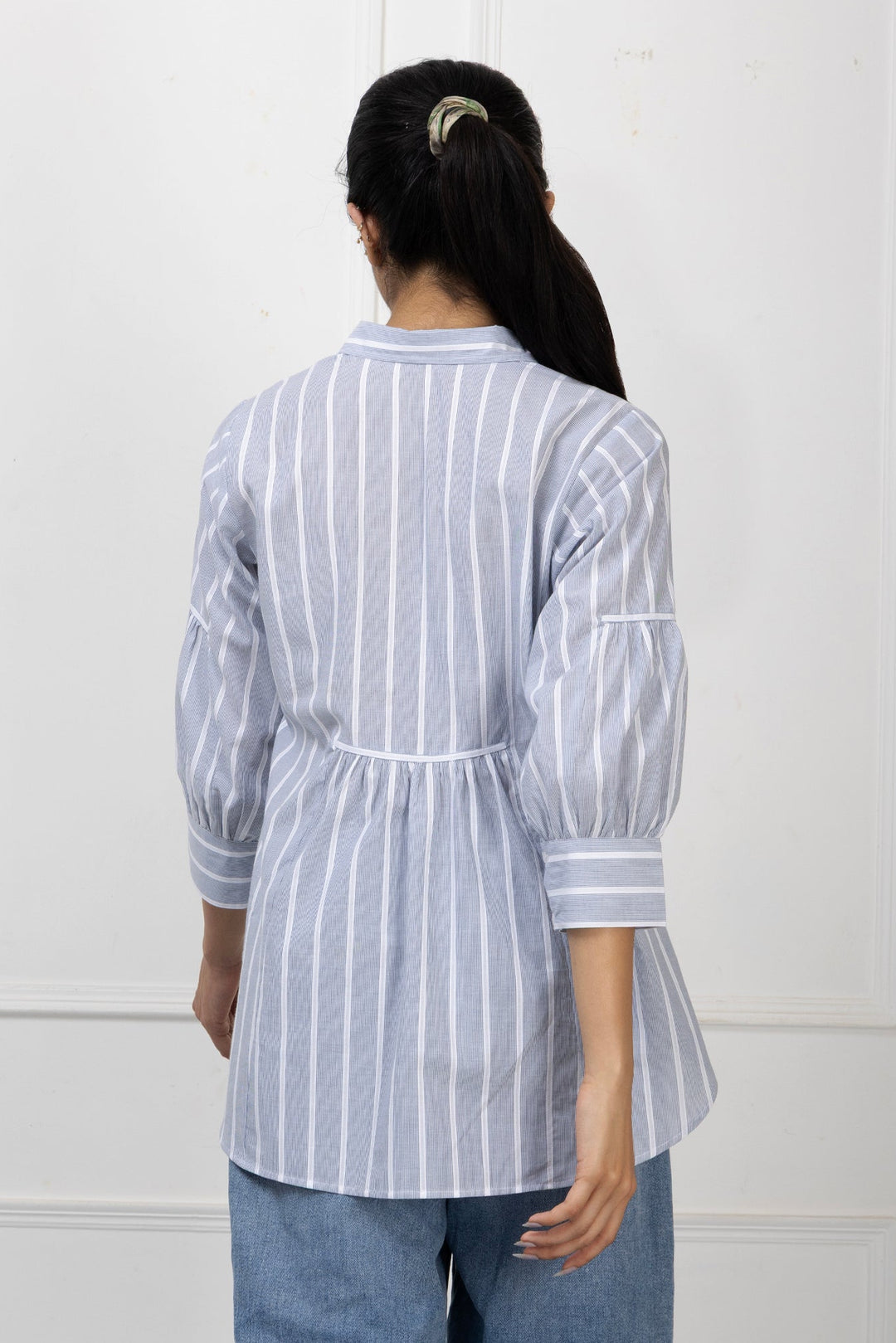 Person wearing a white and blue striped shirt with a plain background