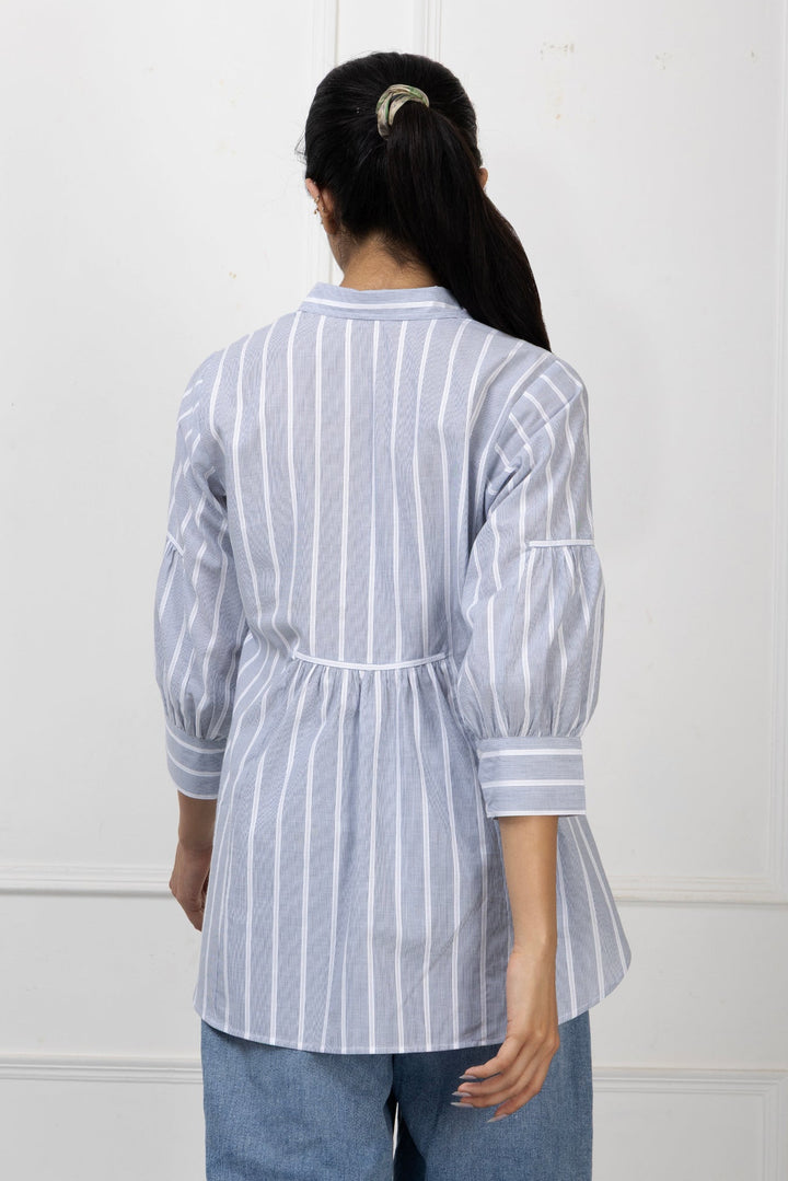 Person wearing a white and blue striped shirt with a plain background