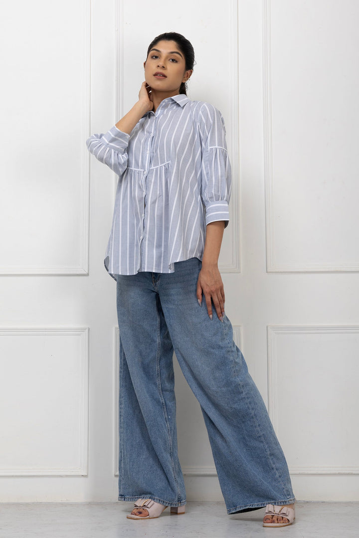 Woman wearing a striped shirt and wide-leg jeans against a white paneled wall.