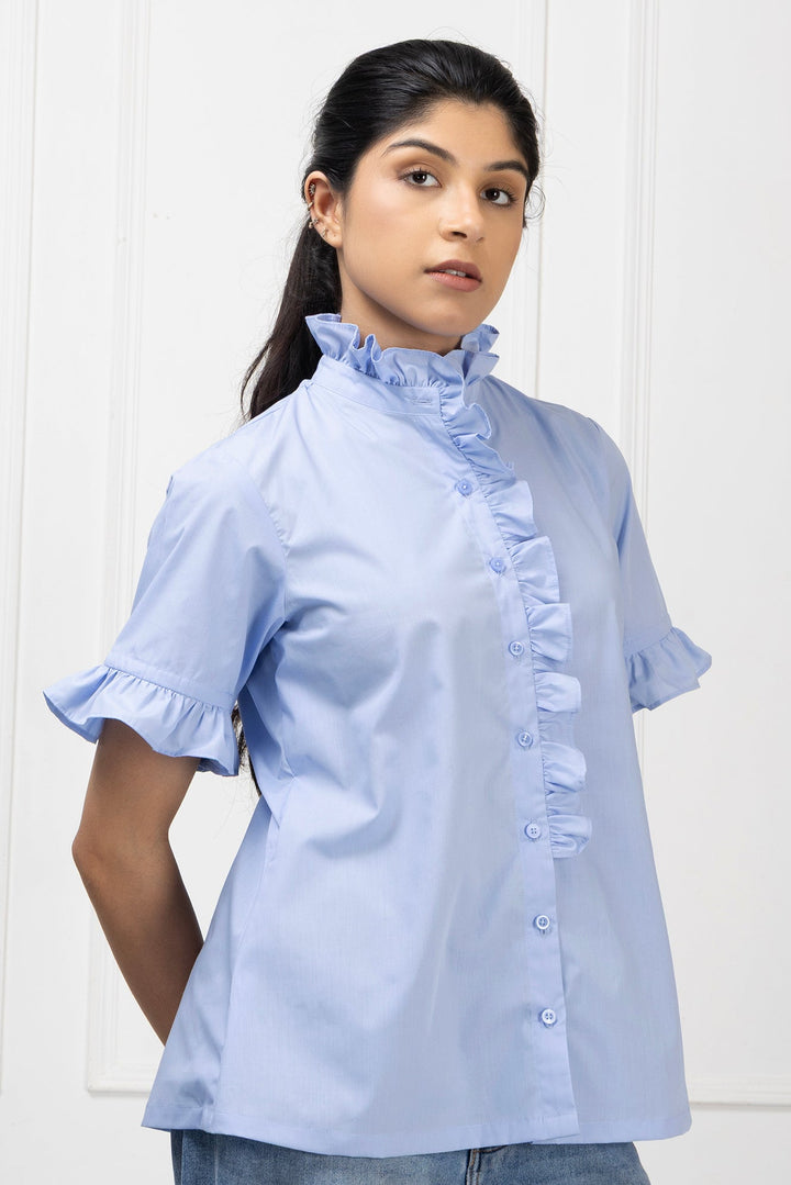 Woman wearing a light blue blouse with ruffled details against a white background