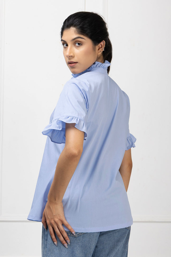 Woman wearing a light blue blouse with ruffled sleeves against a white background