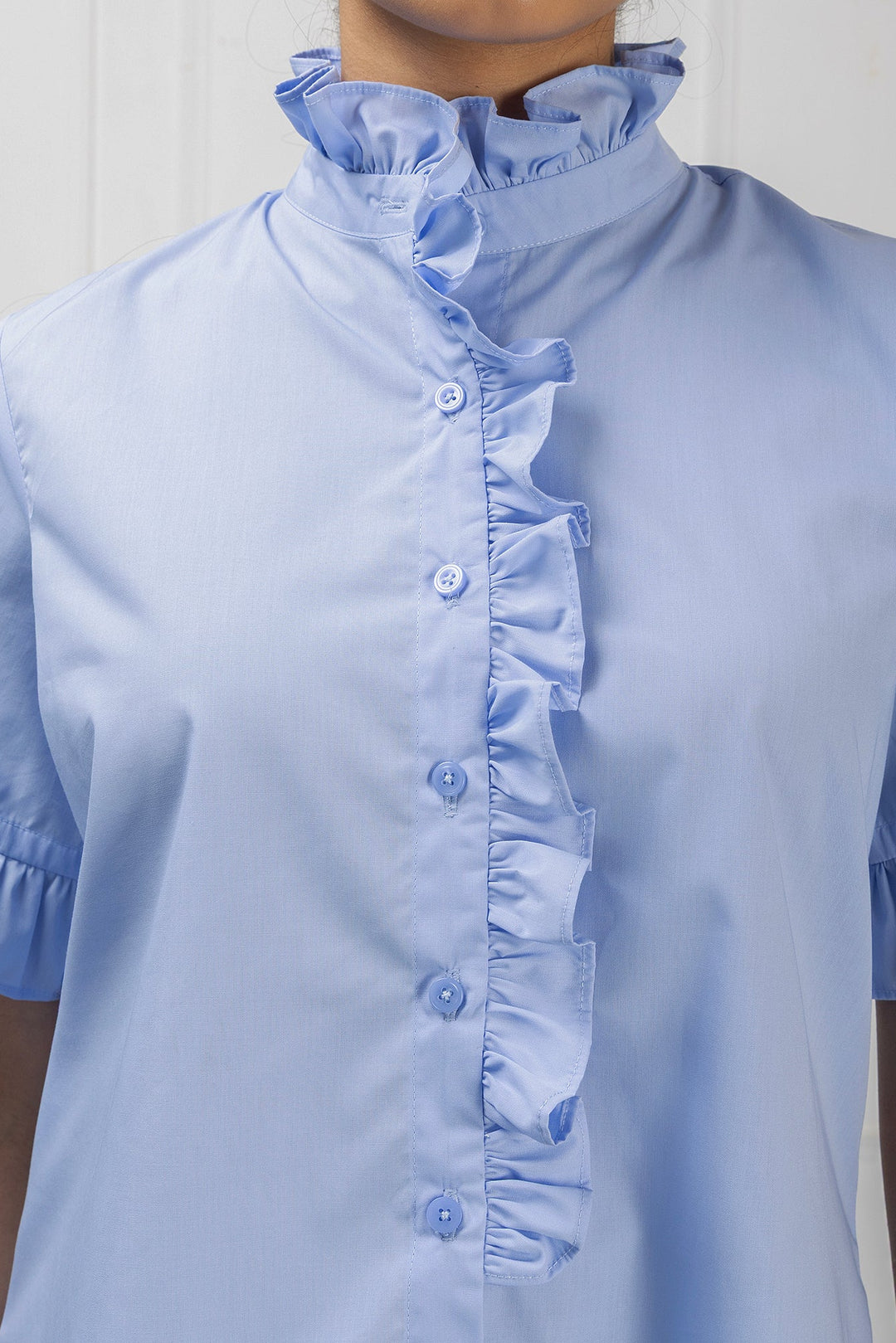 Light blue blouse with ruffled collar and cuffs on a plain background