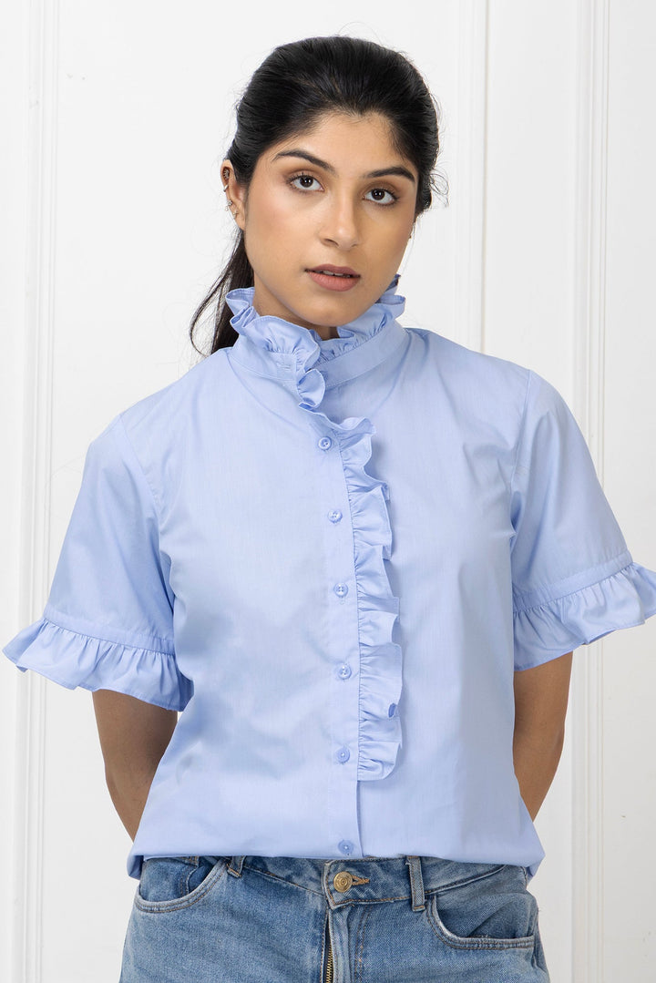 Woman wearing a light blue blouse with ruffled details against a white background