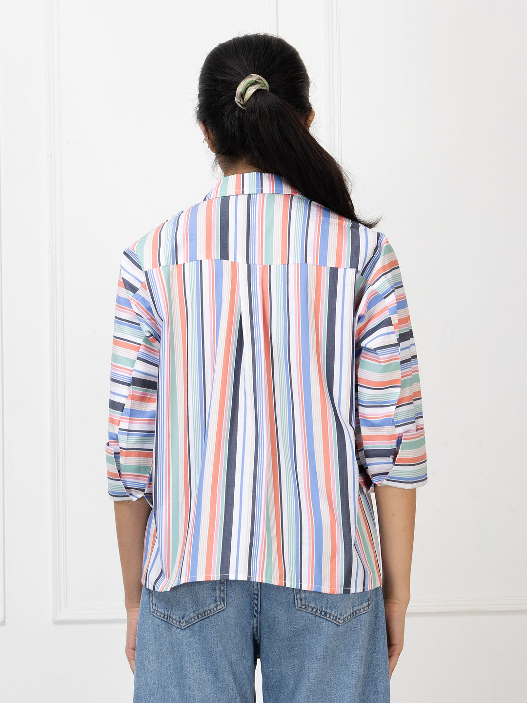 Person wearing a multicolored striped shirt and blue jeans against a white background