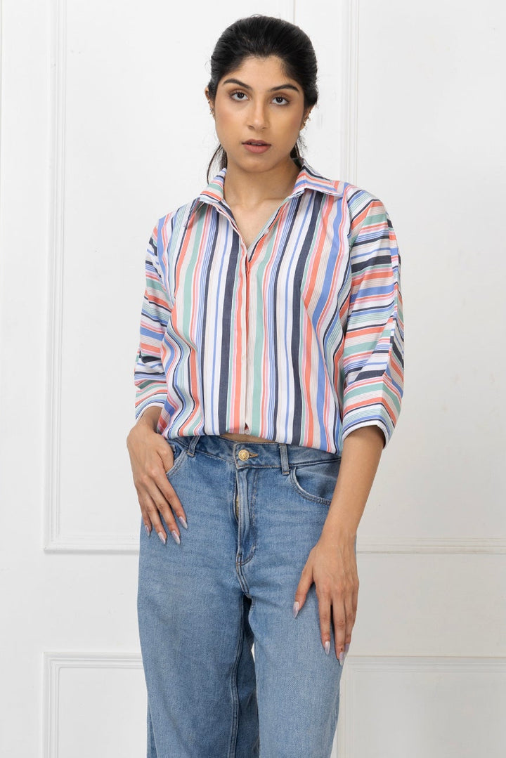 Woman wearing a striped shirt and blue jeans against a white paneled wall.