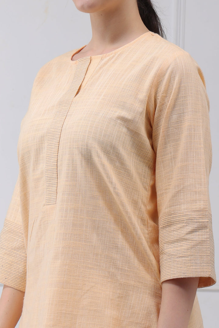 A close-up of a woman wearing a light peach-colored textured tunic or kurta with three-quarter sleeves and a split neckline.