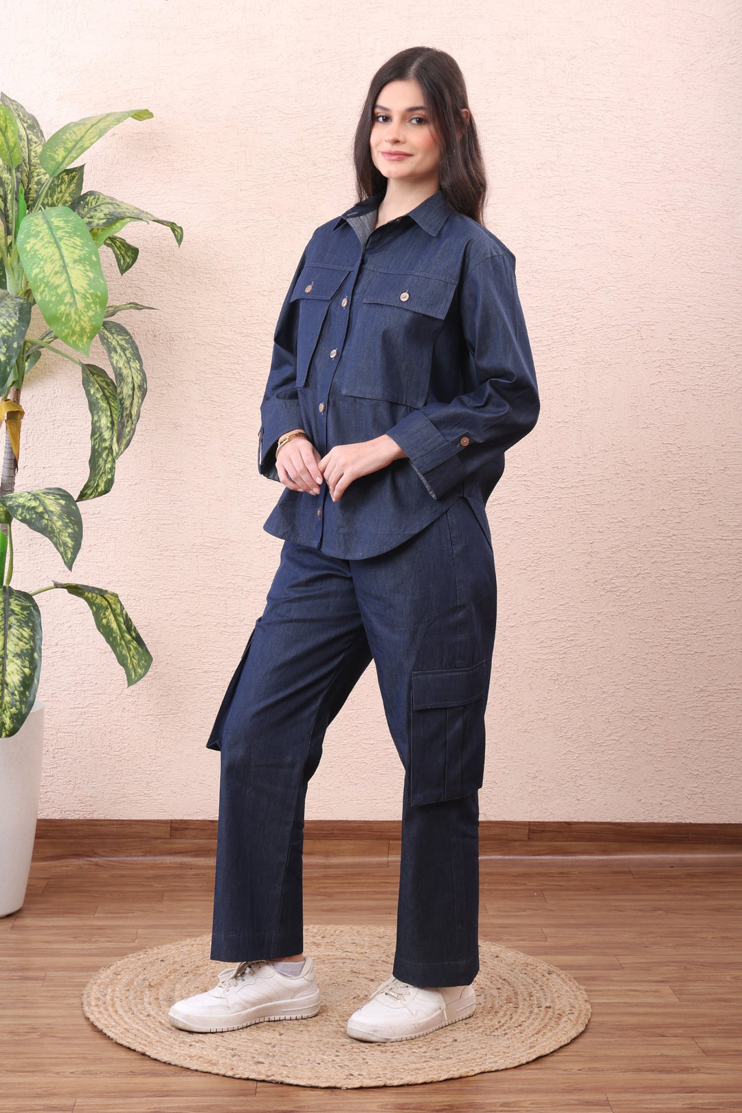 Woman wearing a navy blue outfit standing next to a plant indoors.