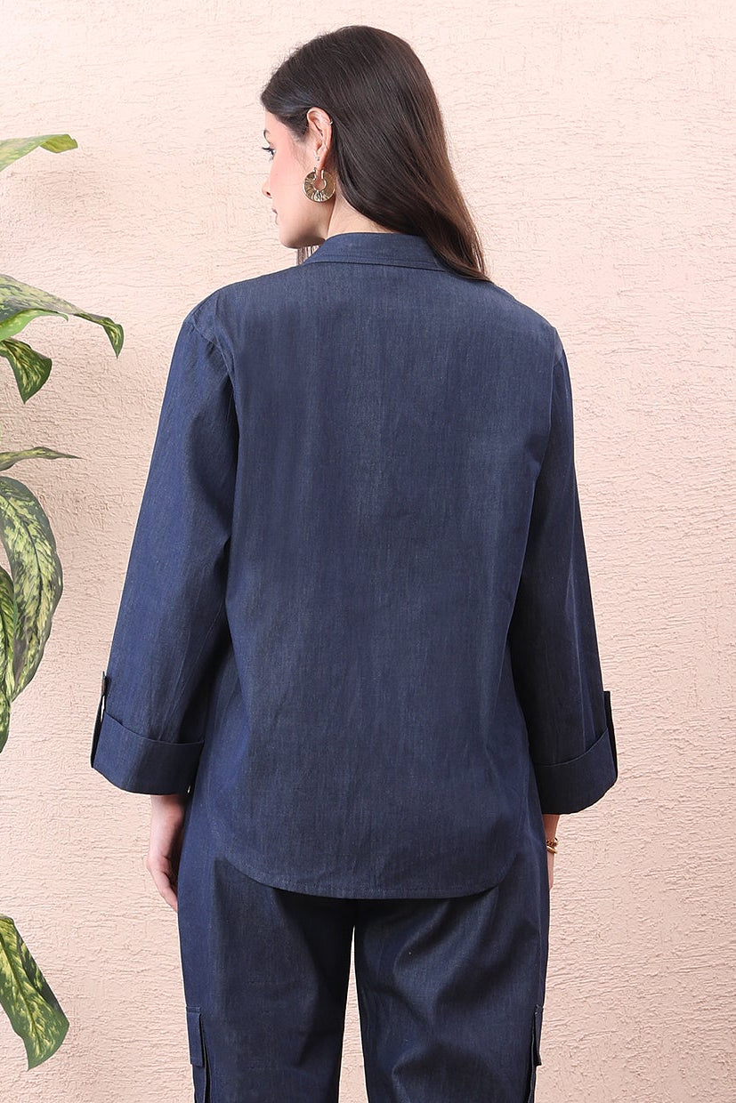 Person wearing a navy blue outfit standing in a room with a plant and wooden floor.