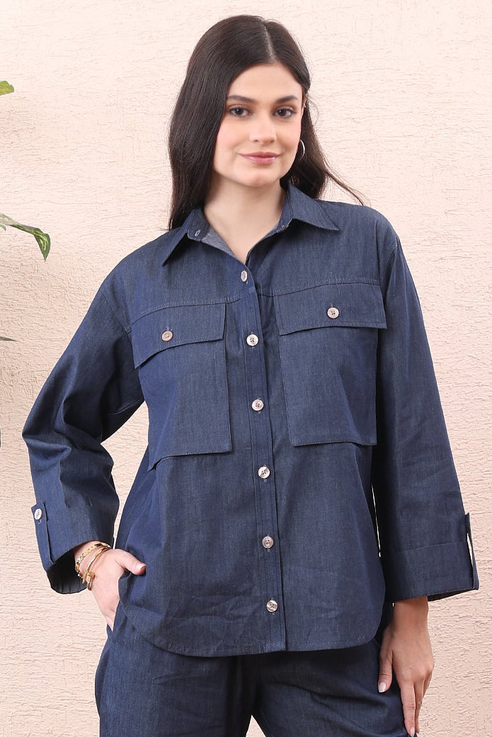 Woman wearing a navy blue outfit standing in a room with a plant and wooden floor.