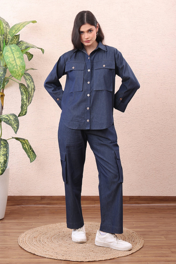 Woman wearing a navy blue outfit standing next to a potted plant indoors.