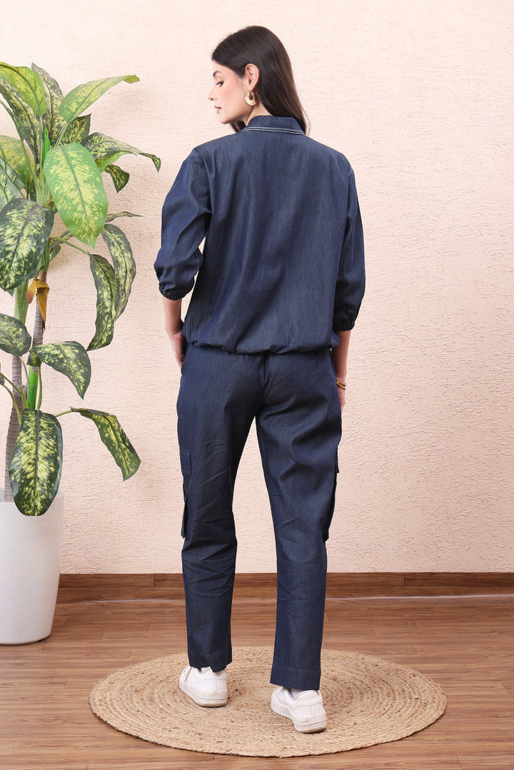 Woman wearing a navy blue outfit standing in a room with a plant and wooden floor.