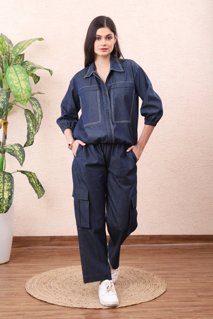 Woman wearing a dark blue denim outfit standing in a room with a plant and rug.