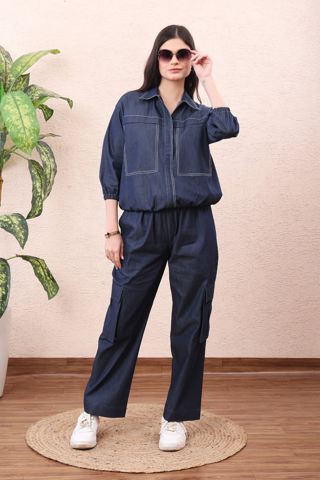 Woman wearing a blue denim outfit standing next to a plant indoors.