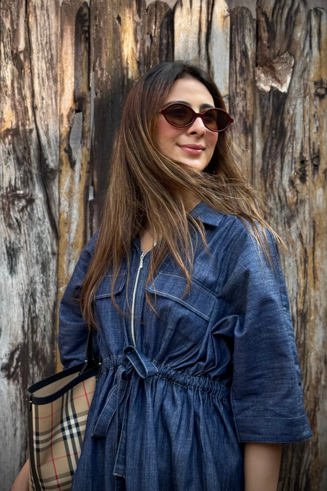 Woman wearing a blue denim co-ord set and sunglasses against a wooden fence.