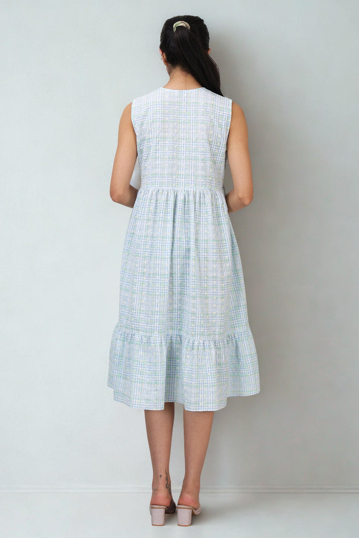 Woman wearing a light blue checkered dress against a plain background