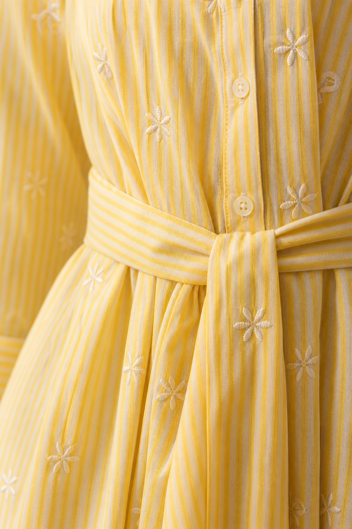 Close-up of a yellow dress with floral patterns and a belt.