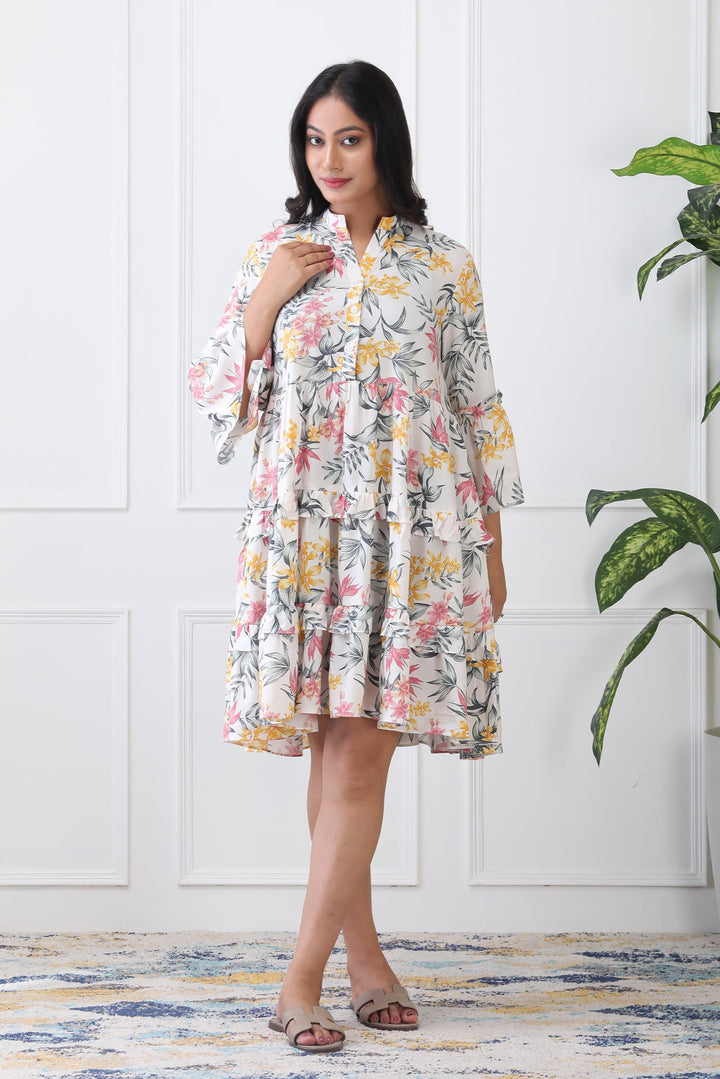 Woman wearing a floral dress standing in a room with a plant and white paneled wall.