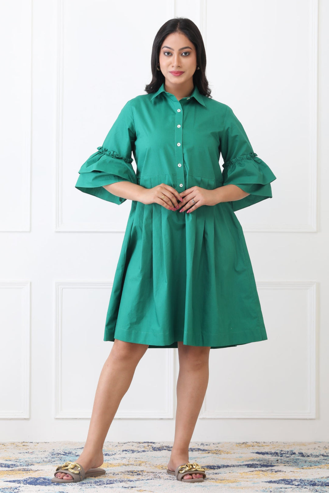 Woman wearing a green dress standing against a white paneled wall.