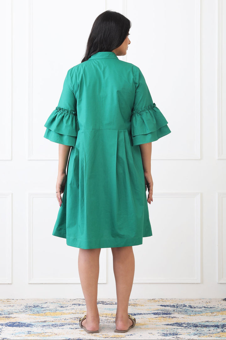 Woman wearing a green dress with ruffled sleeves in a minimal indoor setting