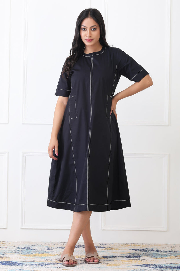 Woman wearing a black dress with white stitching against a white wall.