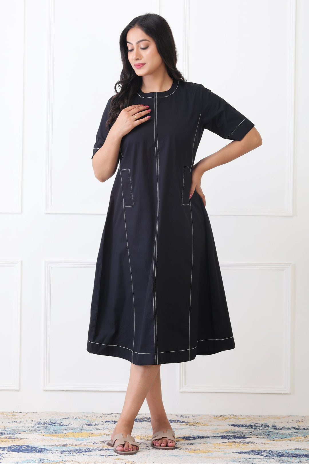 Woman wearing a black dress with white stitching against a white background