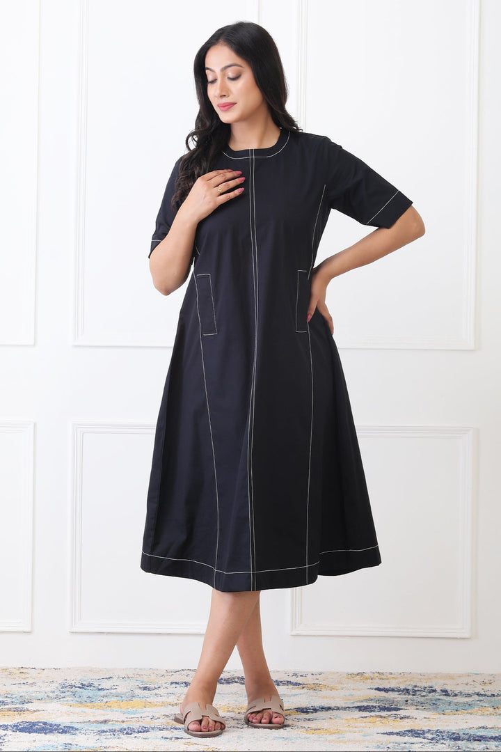 Woman wearing a black dress with white stitching against a white background