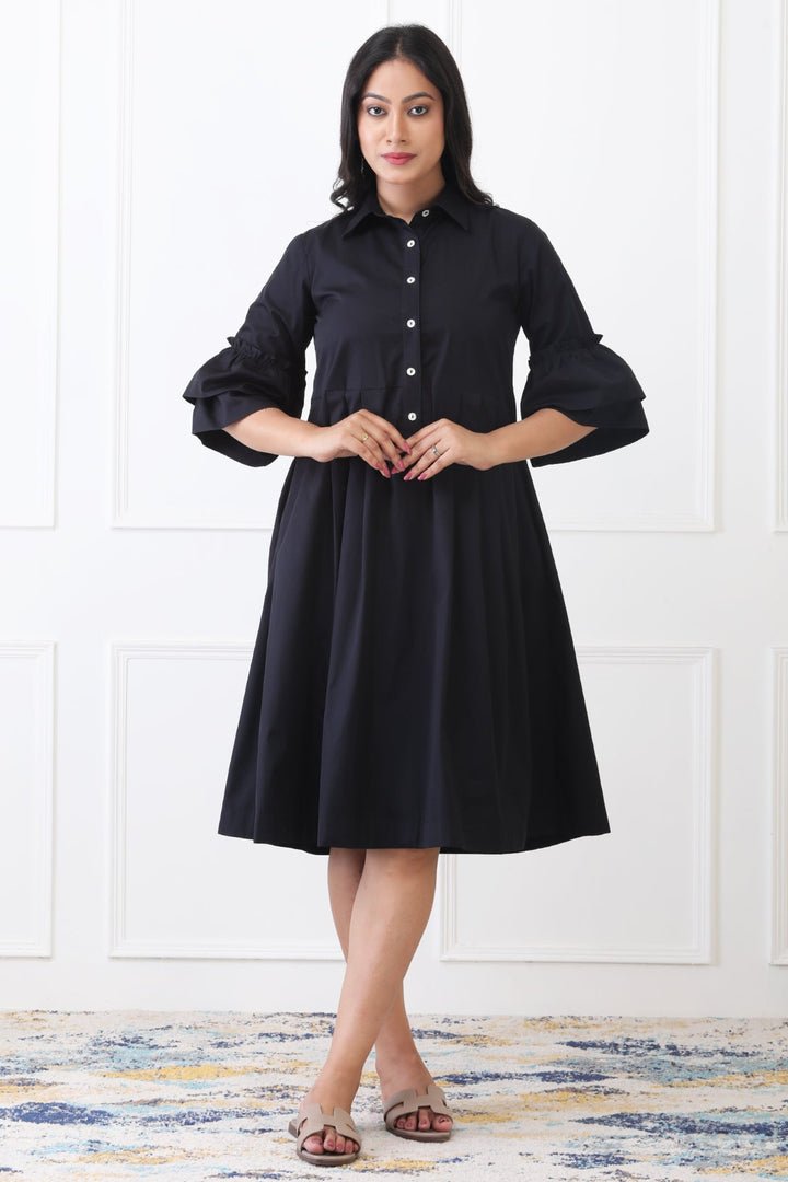 Woman wearing a black dress standing against a white paneled wall.