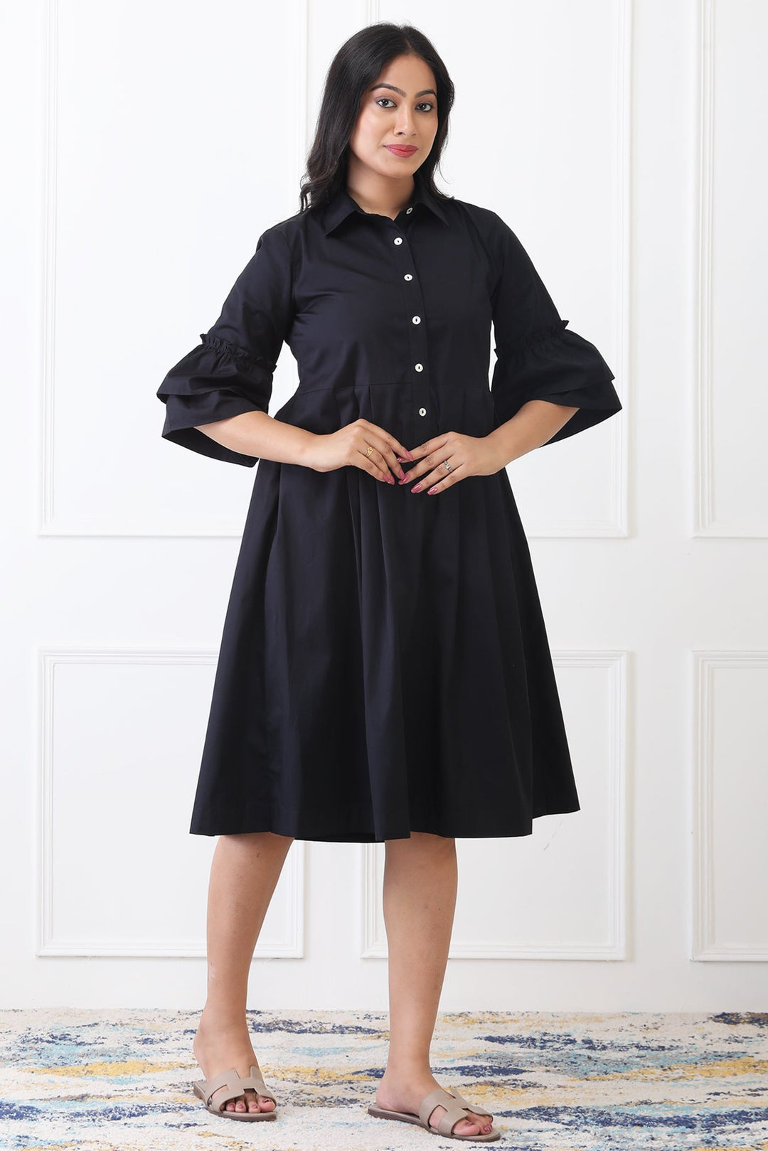 Woman wearing a black dress standing against a white wall.