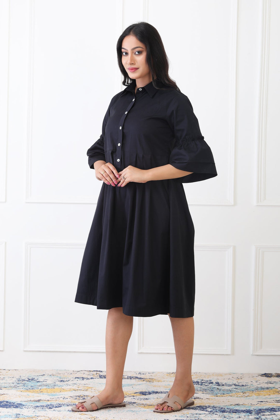 Woman wearing a black dress standing against a white paneled wall.