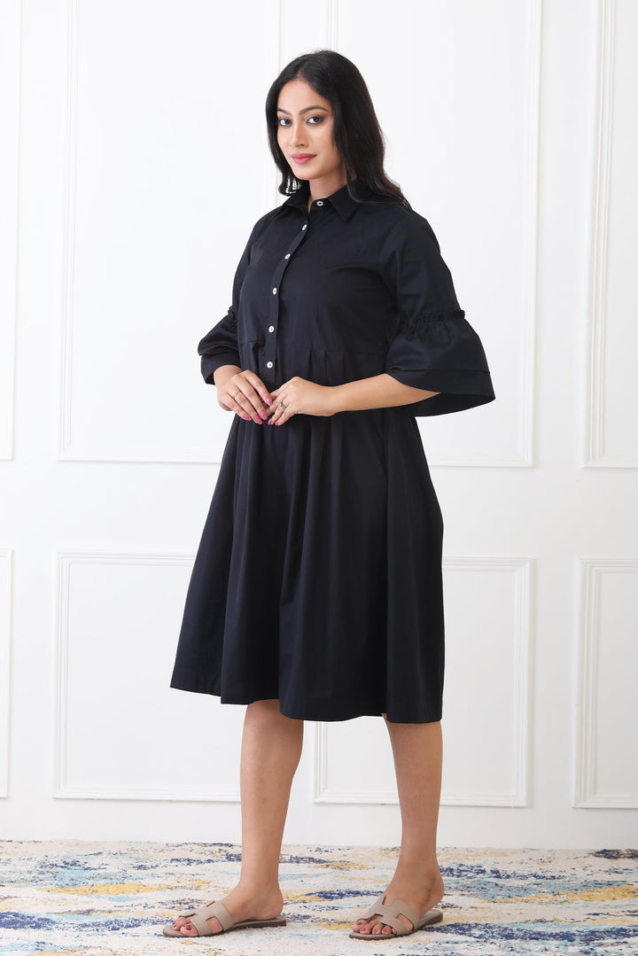 Woman wearing a black dress standing against a white paneled wall.