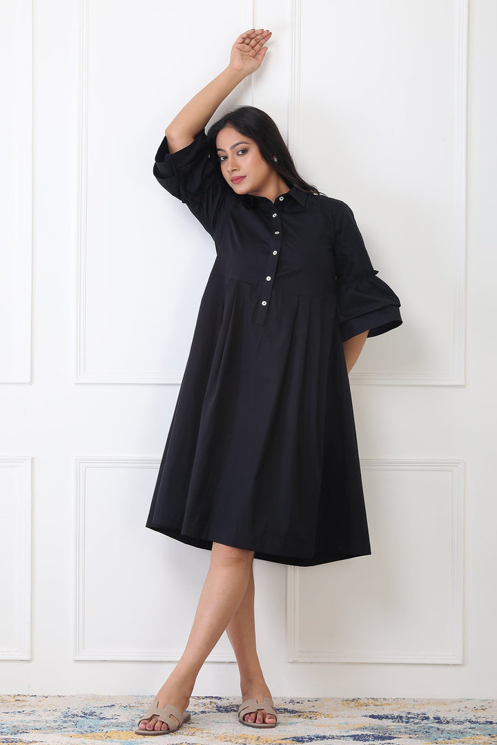 Woman wearing a black dress against a white paneled wall
