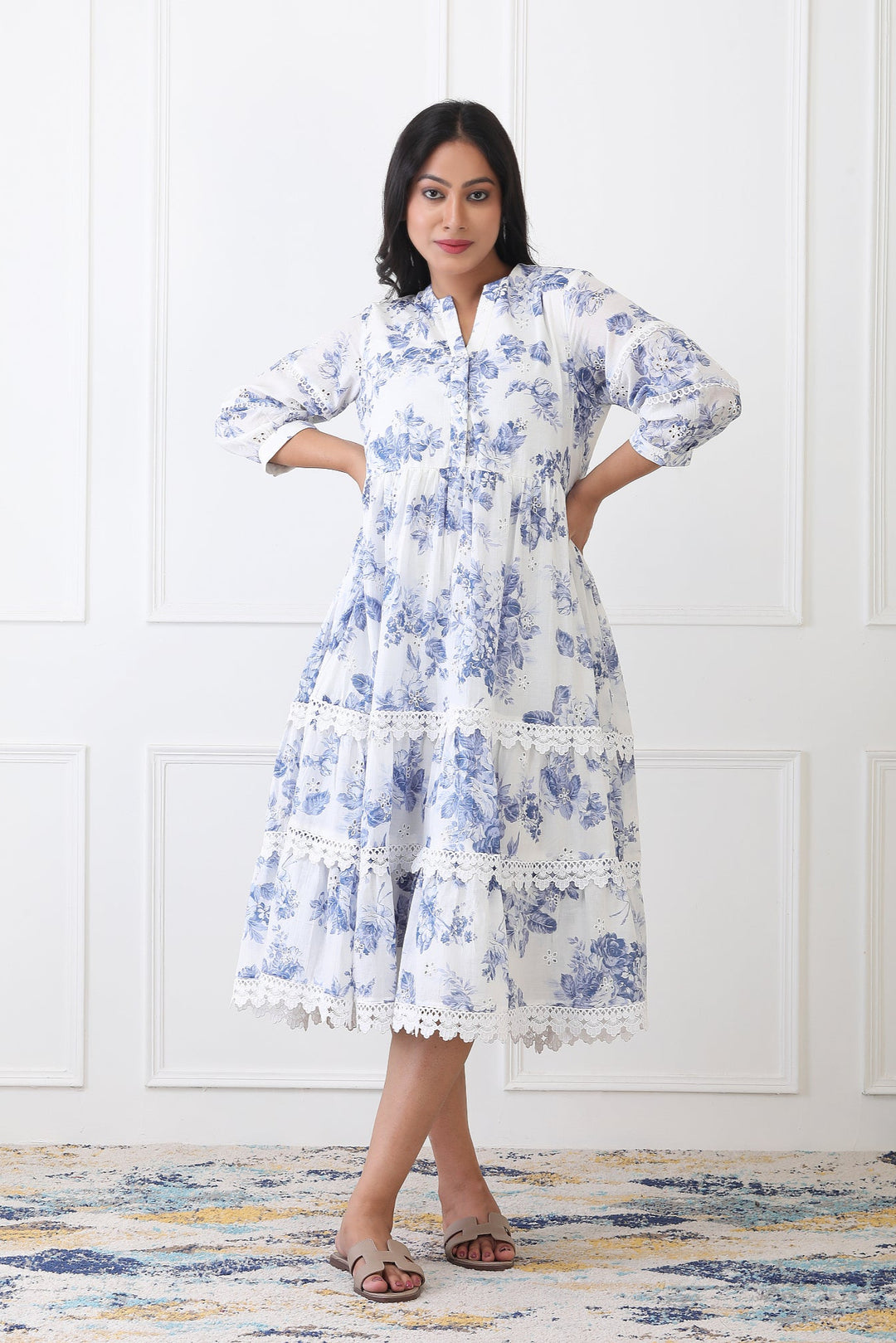 Woman wearing a blue floral dress standing against a white wall.