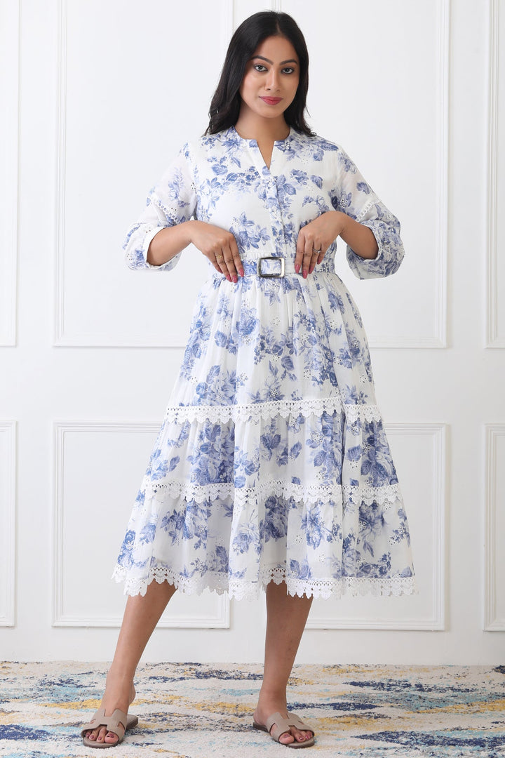 Woman wearing a blue floral dress standing against a white paneled wall.
