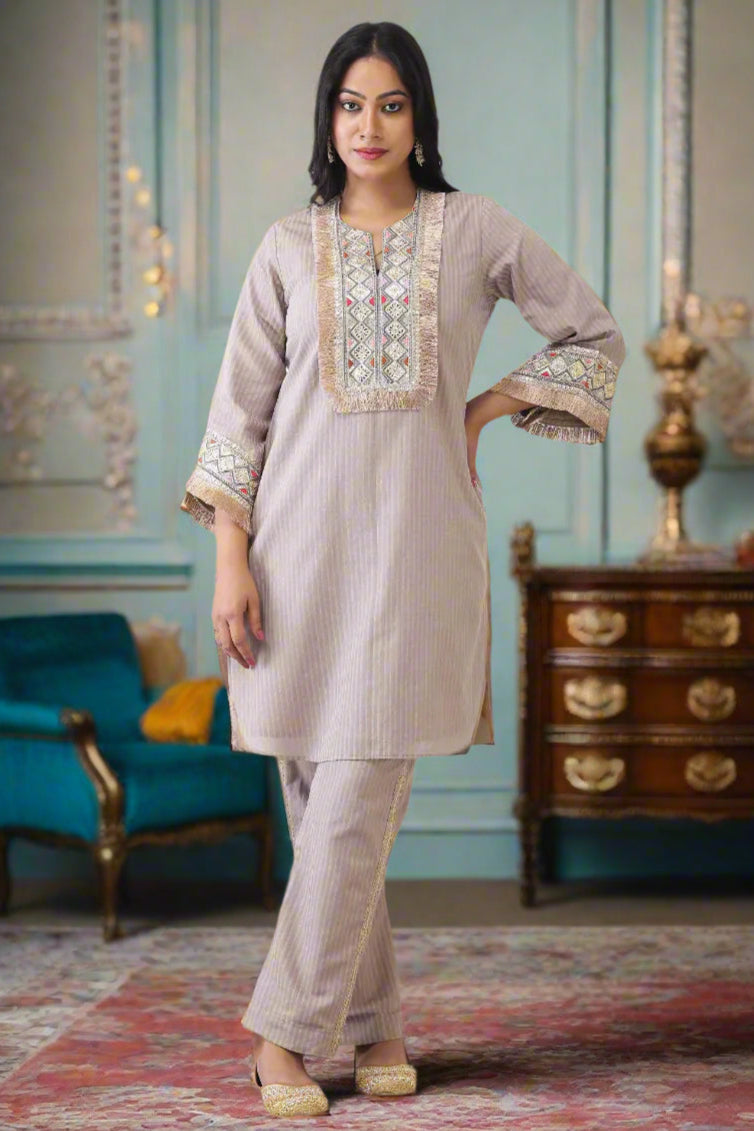 Woman wearing a beige embroidered outfit on a white paneled wall background
