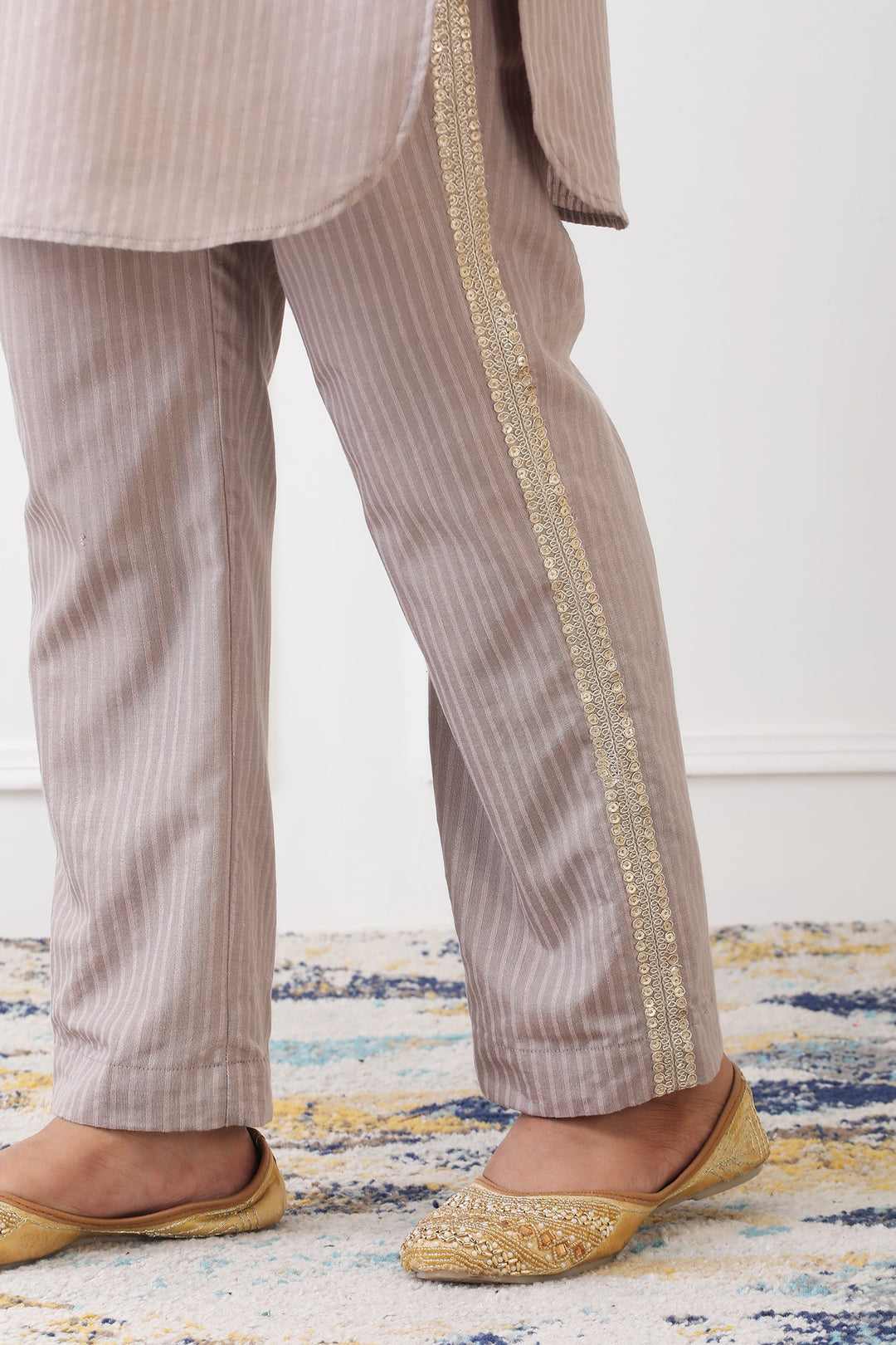 Striped pants with gold trim worn by a person on a patterned rug.