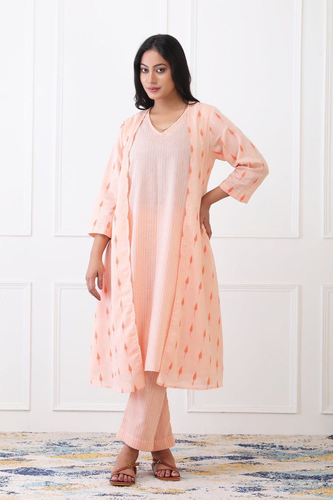 Woman wearing a peach kurta with a matching dupatta against a white wall.