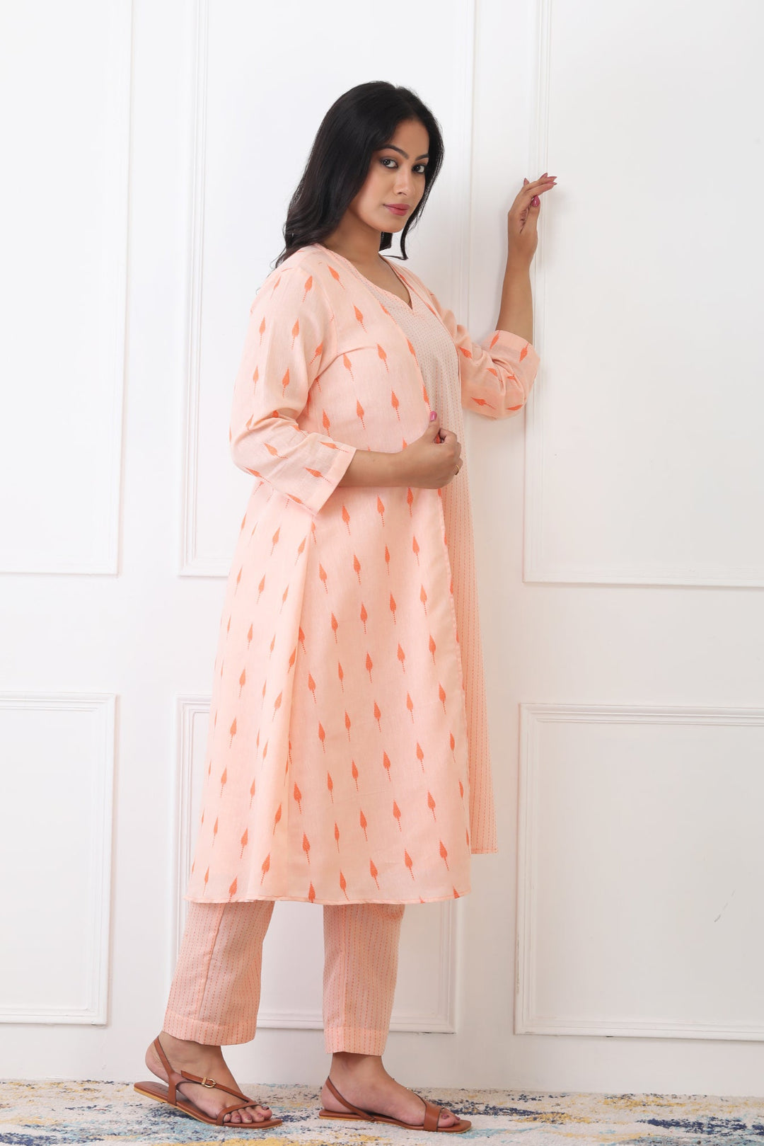 Woman wearing a peach-colored dress with a subtle pattern against a white wall.