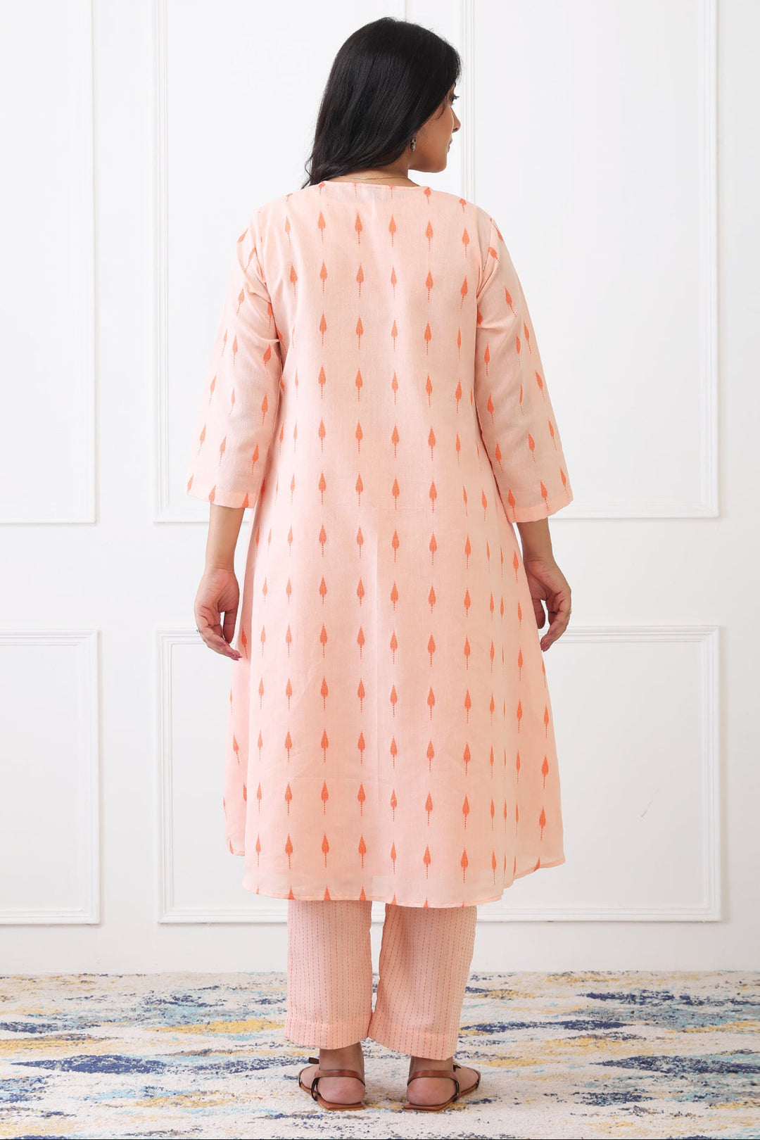 Woman wearing a peach-colored kurta with white patterns against a white wall.