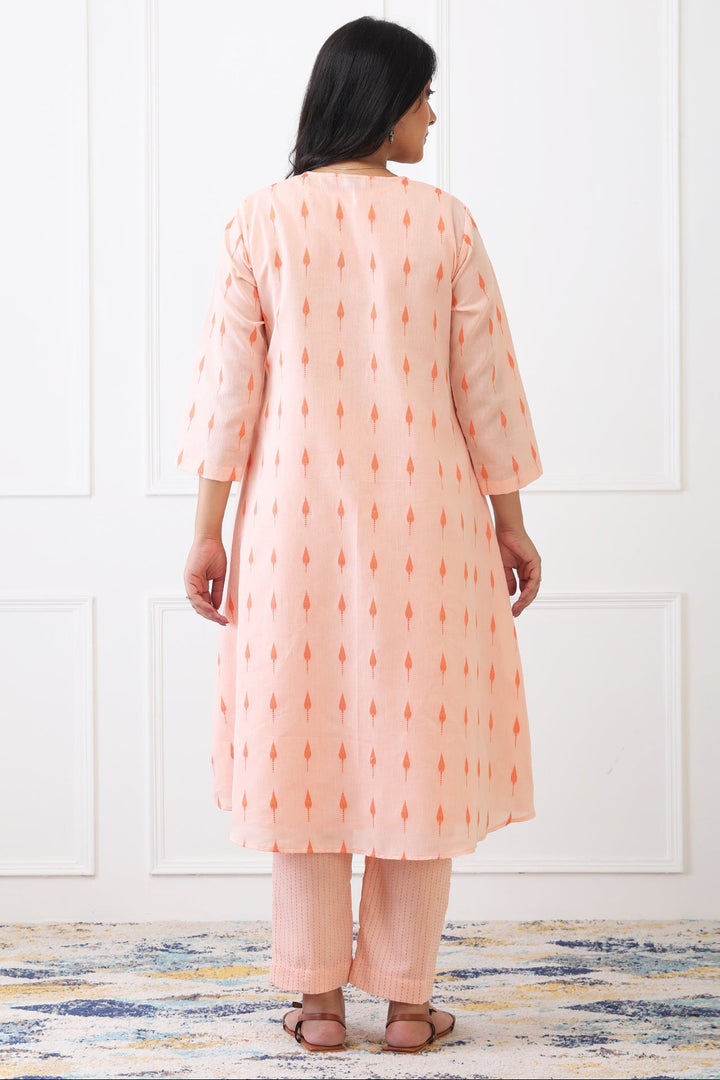 Woman wearing a peach-colored kurta with white patterns against a white wall.
