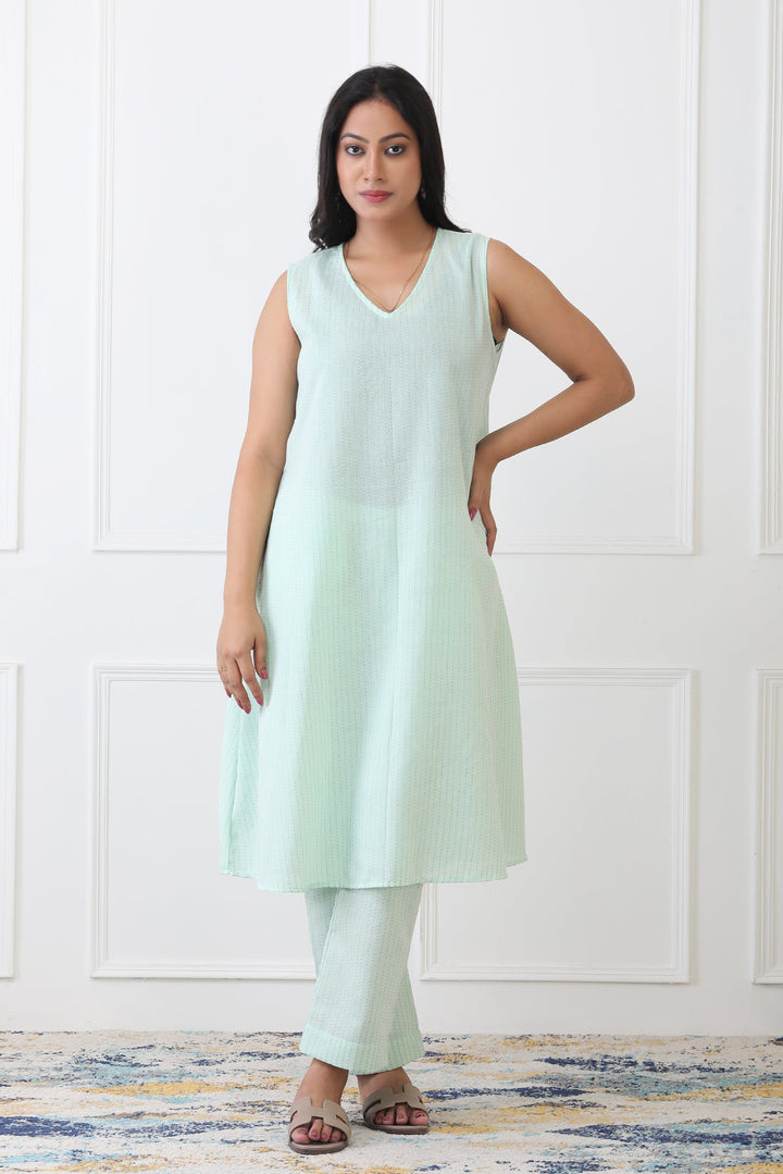 Woman wearing a light green sleeveless top and pants against a white background