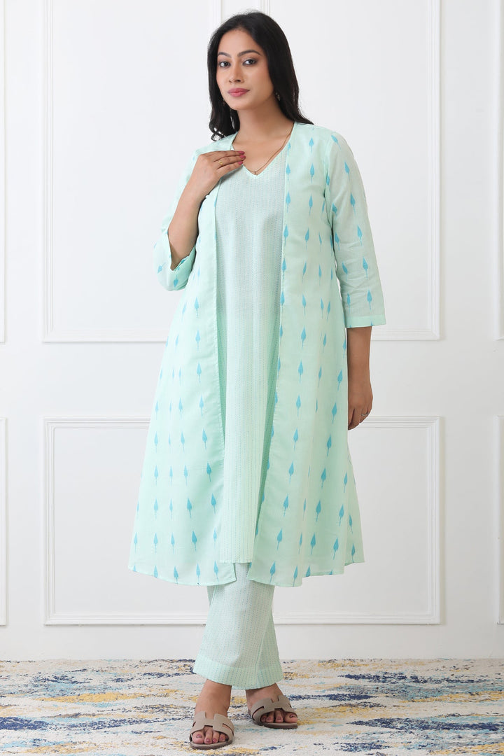 Woman wearing a light green kurta with a matching dupatta against a white paneled wall.