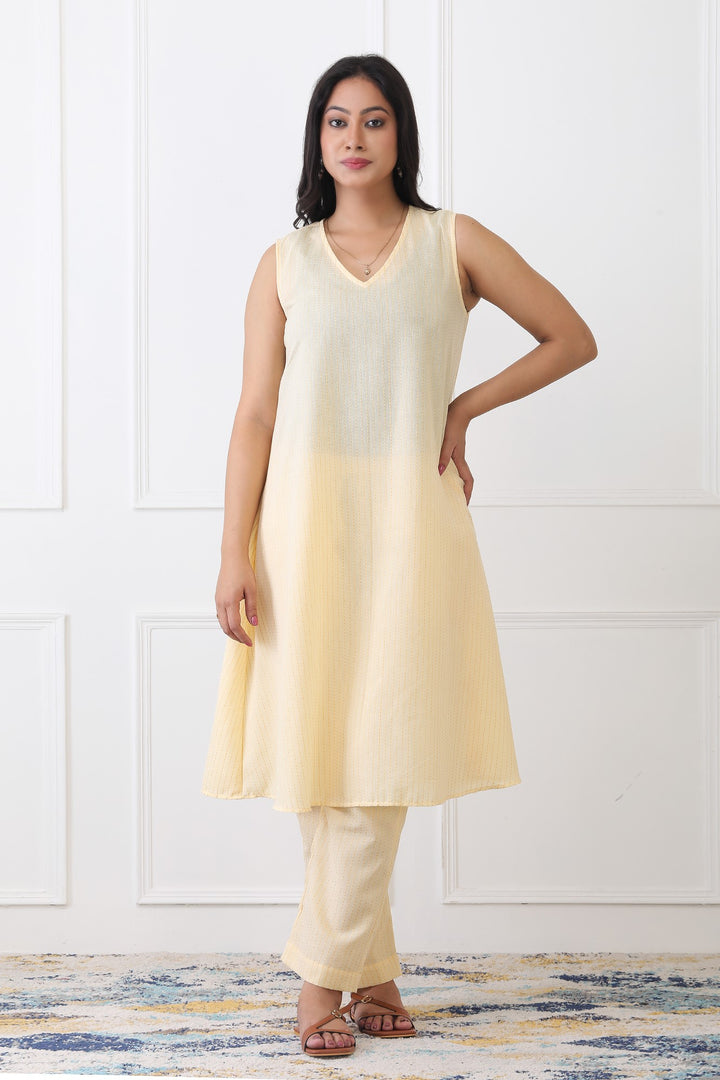 Woman wearing a light yellow sleeveless top and pants against a white background