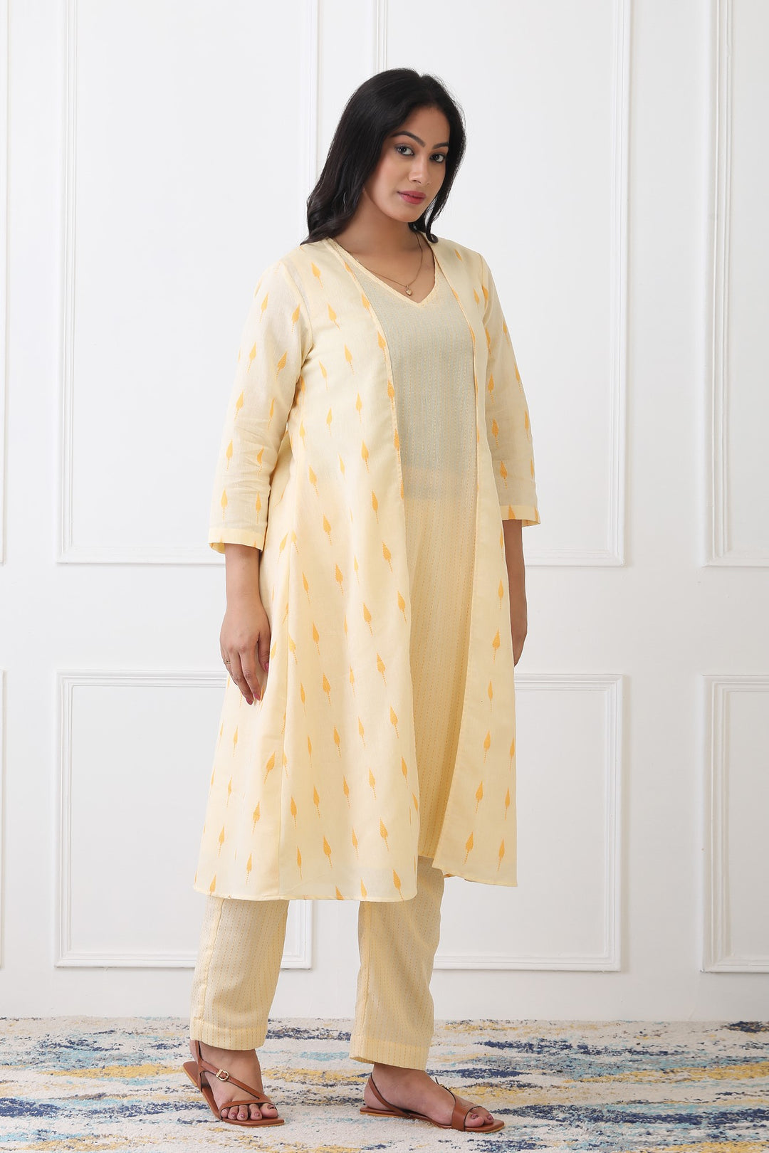 Woman wearing a yellow kurta with a matching drape against a white paneled wall.