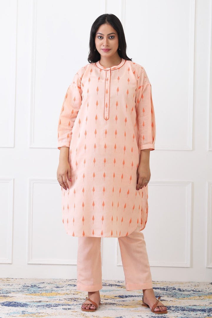 Woman wearing a peach-colored kurta with pants against a white wall.